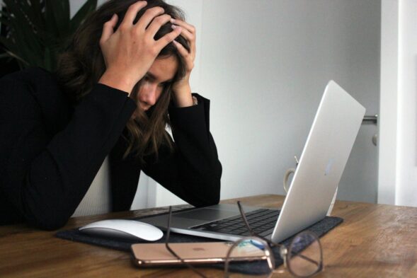 woman in black long sleeve shirt covering her face with her hands in stress