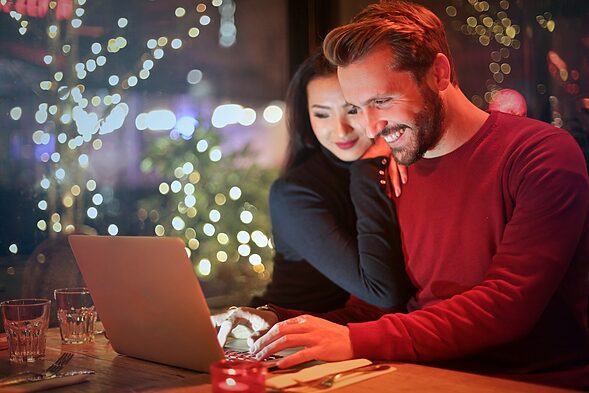 man and woman looking on silver laptop while smiling, romance