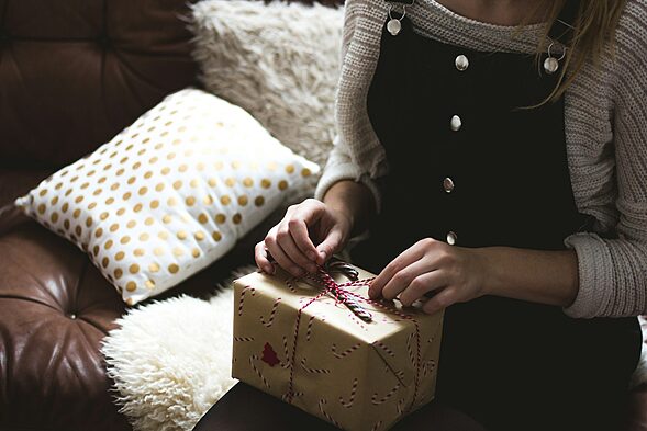 woman in grey sweater and blue denim dungarees sitting on brown and white sofa opening a yellow gift box, valentine