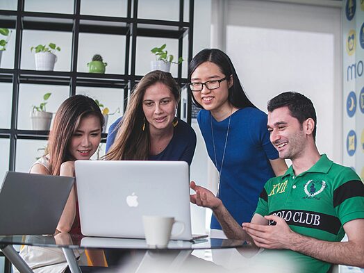 four people watching on white MacBook on top of glass-top table, Office